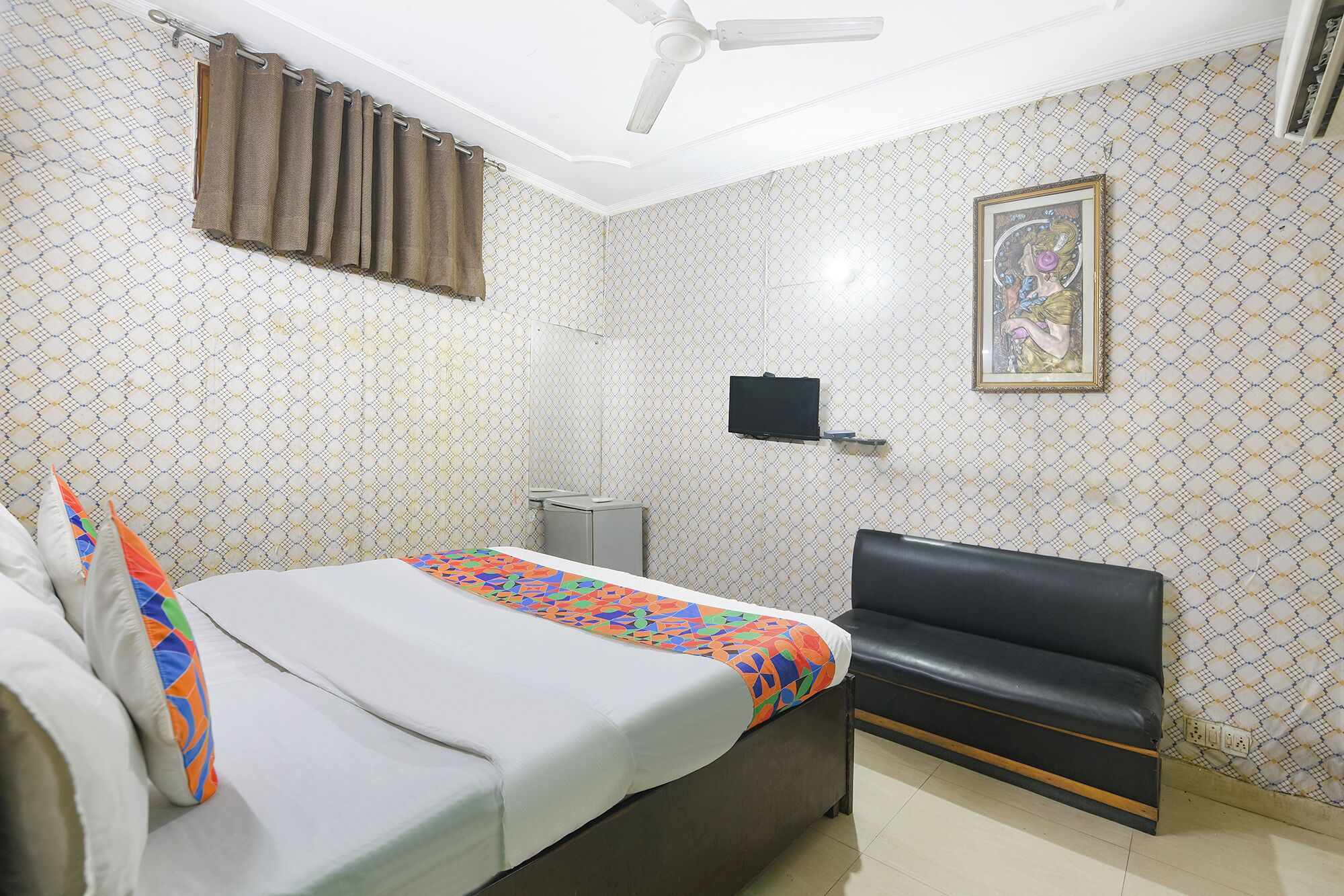 A bedroom with a bed, a sofa, a ceiling fan, a TV, and patterned wallpaper.