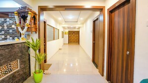 A hotel hallway with a reception desk, a green potted plant, and wooden doors. - Fabhotel Arsh Executive Inn (Kalyan)