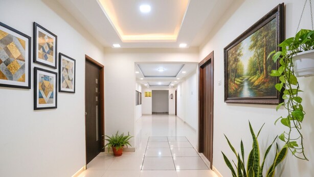 A hallway with a tiled floor, framed artwork on the walls, and potted plants. - Fabhotel Arsh Executive Inn (Kalyan)