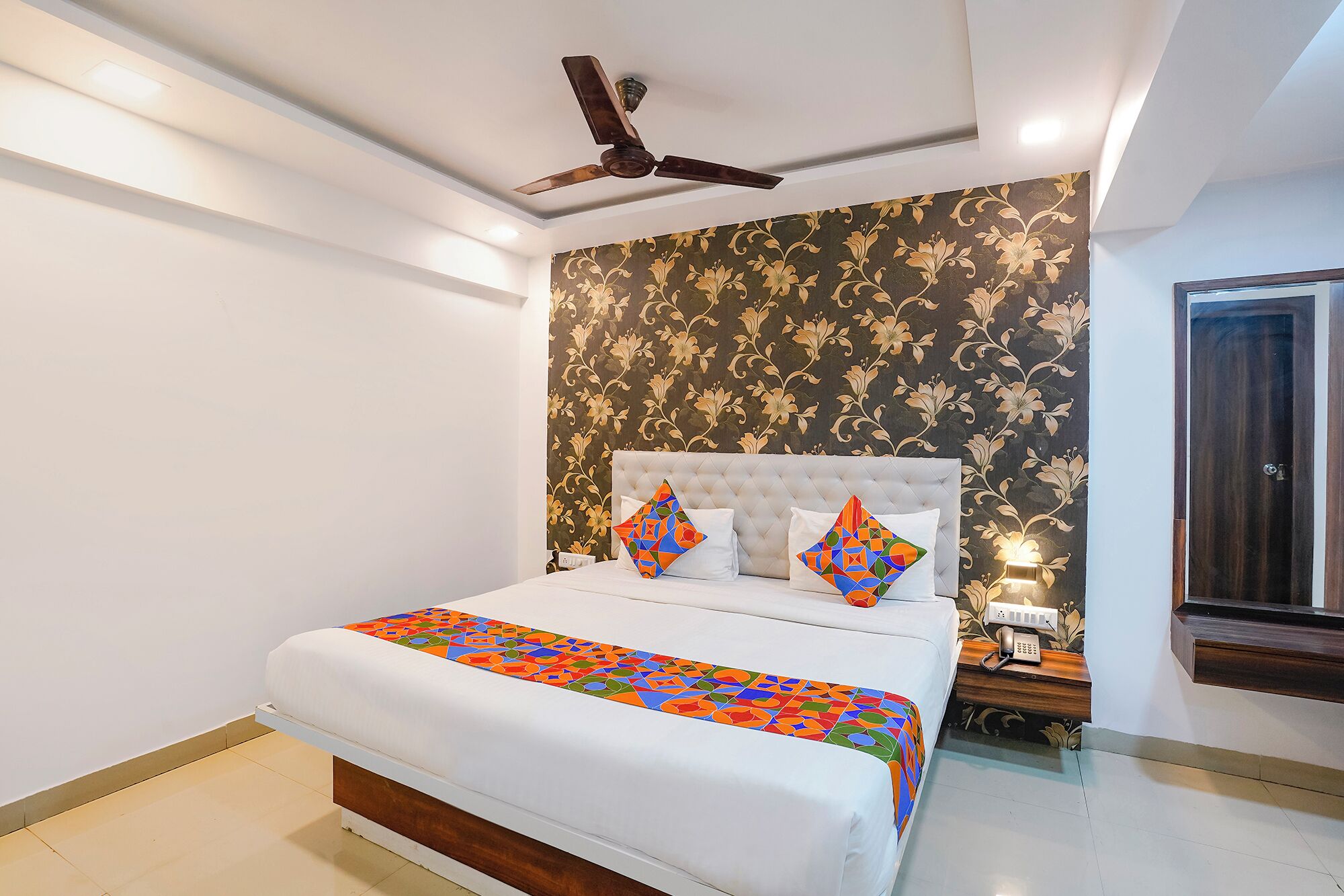 Un dormitorio con cama, ventilador de techo, pared con estampado floral y teléfono junto a la cama.