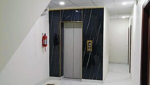 A hallway with a marble wall, a fire extinguisher, and an elevator door. - Fabhotel Red Pepper (Faridabad)