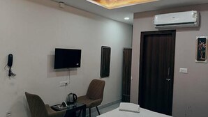 A hotel room with a flat-screen TV, two chairs, a table with a kettle, a door, and an air conditioning unit. - Fabhotel Red Pepper (Faridabad)