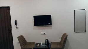 A room with a flat-screen TV mounted on the wall, two brown chairs, a small table with a kettle, and a telephone. - Fabhotel Red Pepper (Faridabad)