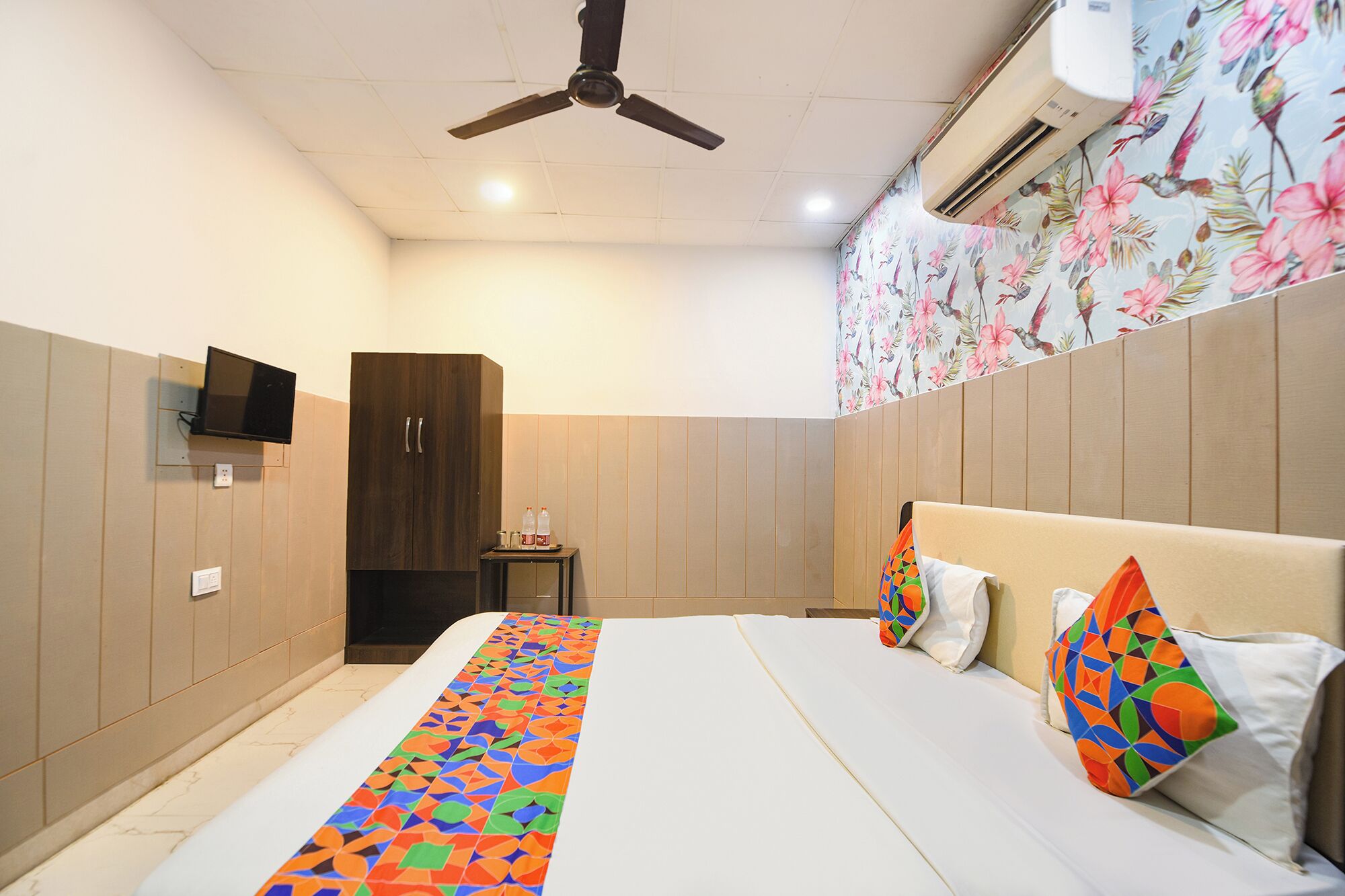 Un dormitorio con una cama, un televisor montado en la pared, un armario y un ventilador de techo.