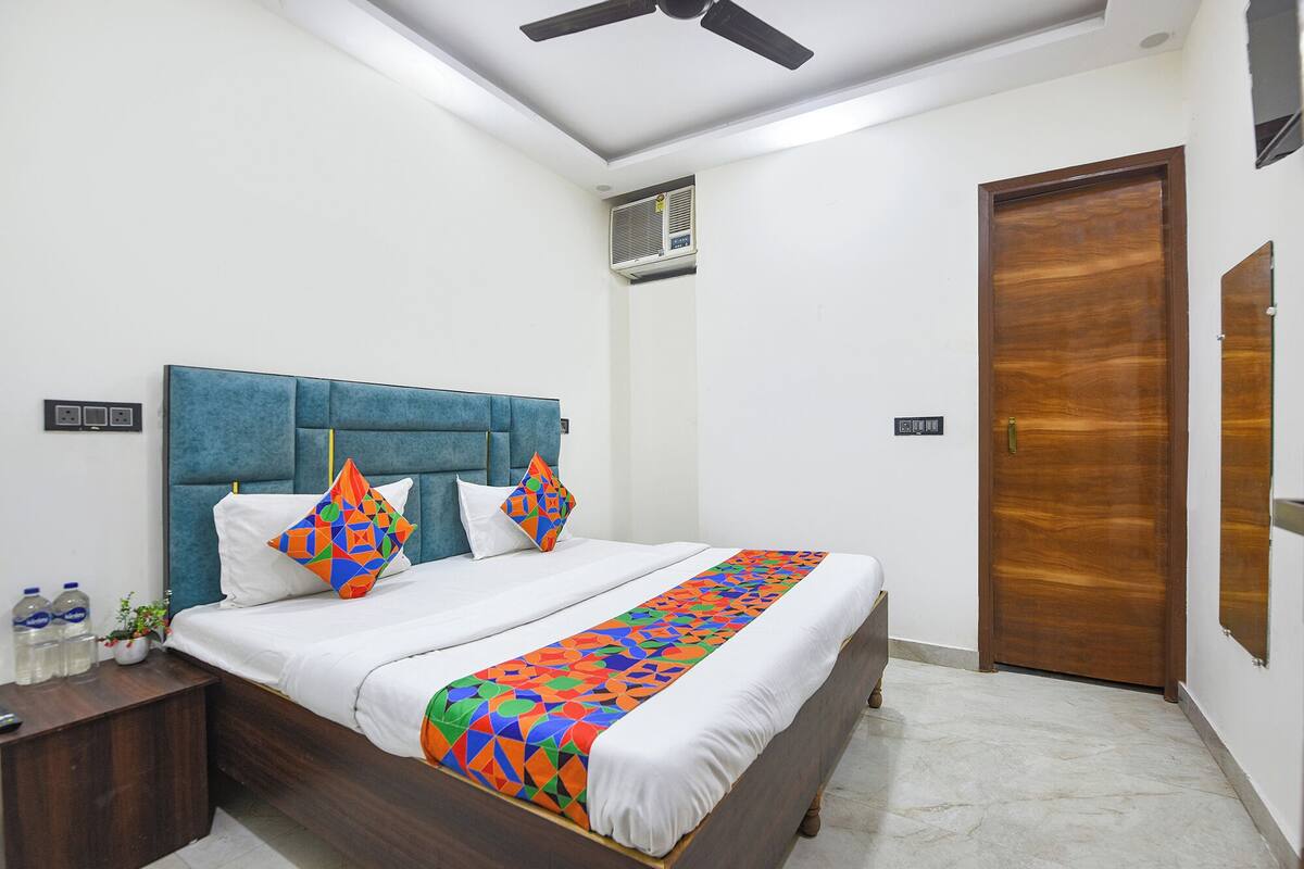 A modern bedroom with a blue upholstered headboard, a white bedspread, and colorful geometric pillows.