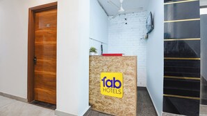 Et reception område med en trædør, en hvid væg med murstensmønster, en ventilator i loftet og et skilt med 'fab hotels'.