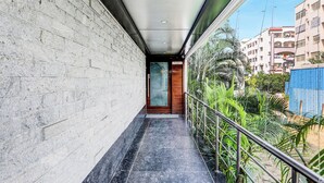 Un couloir étroit, doté d’un sol carrelé, d’une porte en bois et offrant une vue sur un quartier résidentiel avec ses immeubles et sa verdure.