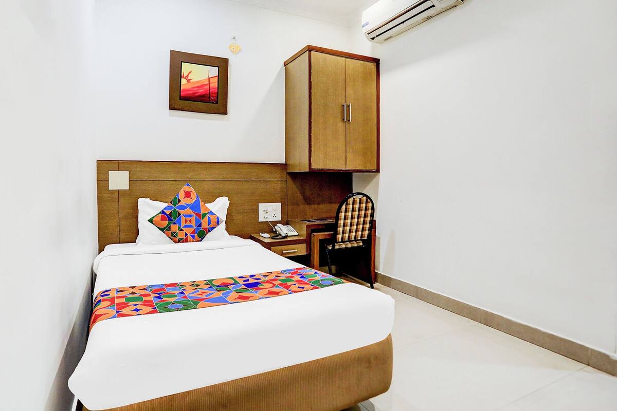 Habitación de hotel con una cama, cabecero de madera, escritorio con silla, armario y equipo de aire acondicionado.