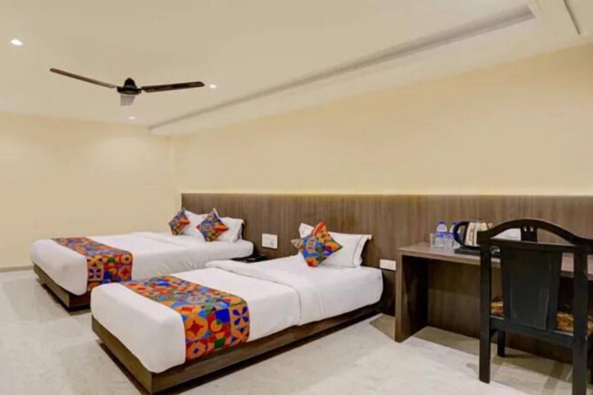 A hotel room with two beds, a ceiling fan, a desk, and a chair.