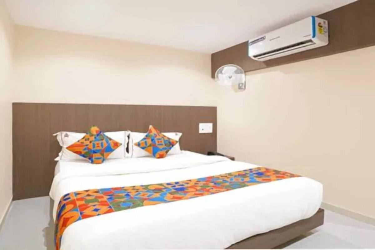 A hotel room with a bed, a wall-mounted air conditioner, and a plain wall.