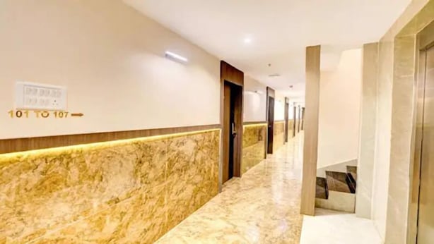 Un couloir d’hôtel avec un sol en marbre, des portes numérotées de 101 à 107 et un panneau indiquant si les chambres sont disponibles.
