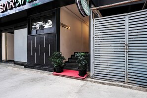 A closed storefront with a reception sign, a black door with vertical handles, and two potted plants on a red mat. - Fabhotel Raayara Bliss (Bangalore)