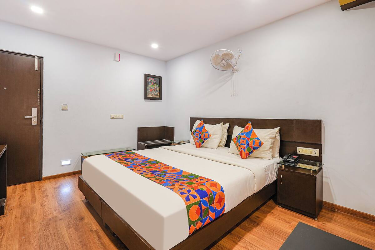 A neatly arranged hotel room with a large bed, bedside tables, a bedside fan, and a small cabinet.