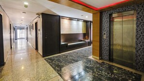 En moderne hotellobby med et marmorgulv, en receptionsdisk og elevator.