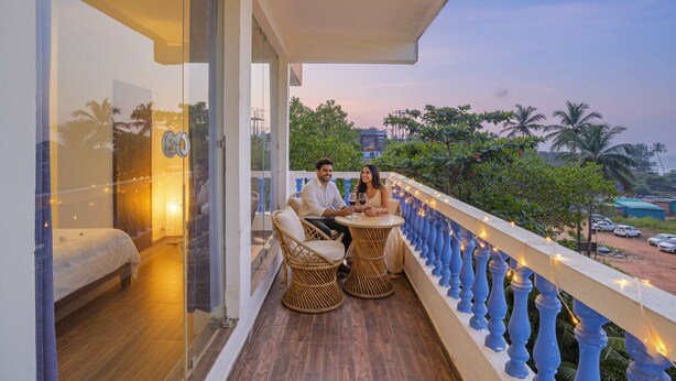 A balcony with wicker furniture and string lights, overlooking a street with parked cars and palm trees. - Via Simba resort - 200m From Arambol Beach (Arambol)
