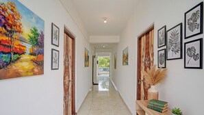 A hallway with a painting, framed botanical prints, a wooden console table with books and a plant, and a tiled floor. - Via Simba resort - 200m From Arambol Beach (Arambol)