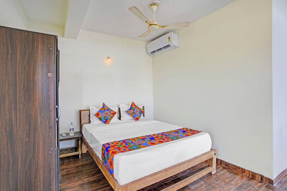 A bedroom with a bed, a wooden wardrobe, a nightstand, a ceiling fan, and an air conditioning unit.