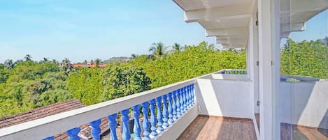 Un balcón con barandilla blanca y balaustradas azules, con vistas a un paisaje verde y exuberante con árboles y cielo despejado.