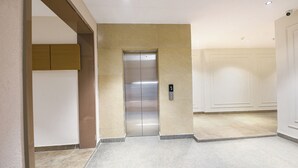 A modern elevator with a metallic finish, a textured beige wall, and a carpeted floor. - FabHotel Prime Elvilla I-@ Rajouri Garden, Delhi (New Delhi)