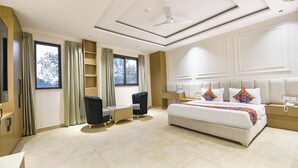 A modern hotel room with a large bed, a desk, and a chair. There is a window with curtains, a ceiling fan, and a nightstand with a phone and a lamp. - FabHotel Prime Elvilla I-@ Rajouri Garden, Delhi (New Delhi)