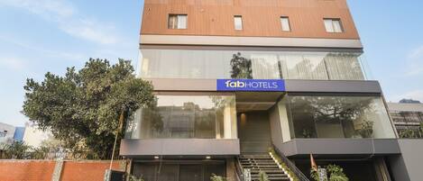 Un edificio moderno con un letrero de 'fabHOTELS', que cuenta con una escalera, una entrada protegida por una reja y plantas en macetas.