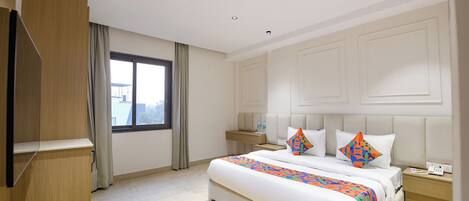 Habitación de hotel con una cama grande, una mesita de noche, un armario, un ventilador de techo, iluminación empotrada y una ventana con cortinas.
