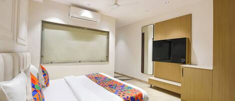 A hotel room with a bed, a large window, an air conditioning unit, a ceiling fan, a TV, and a wooden wardrobe.