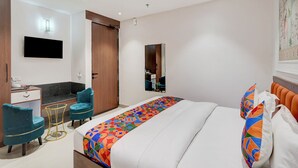 Et hotelværelse med seng, skrivebord, stol, lille bord og spejl.