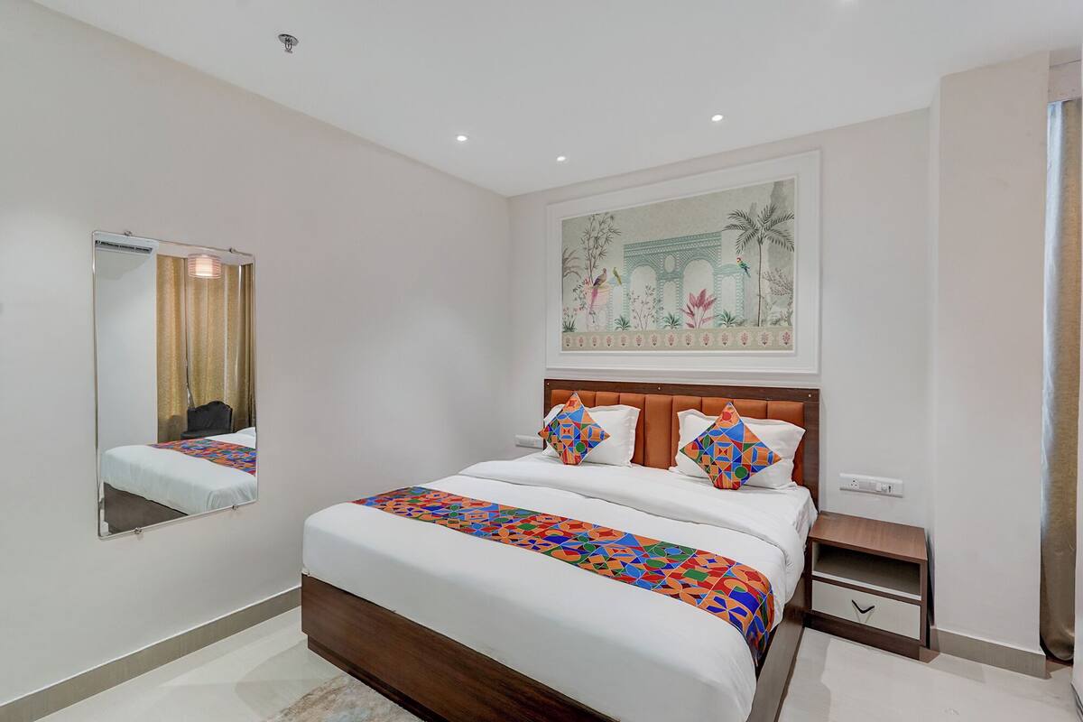 Una habitación de hotel con una cama grande, una mesita de noche, un espejo y una obra de arte colgada en la pared.
