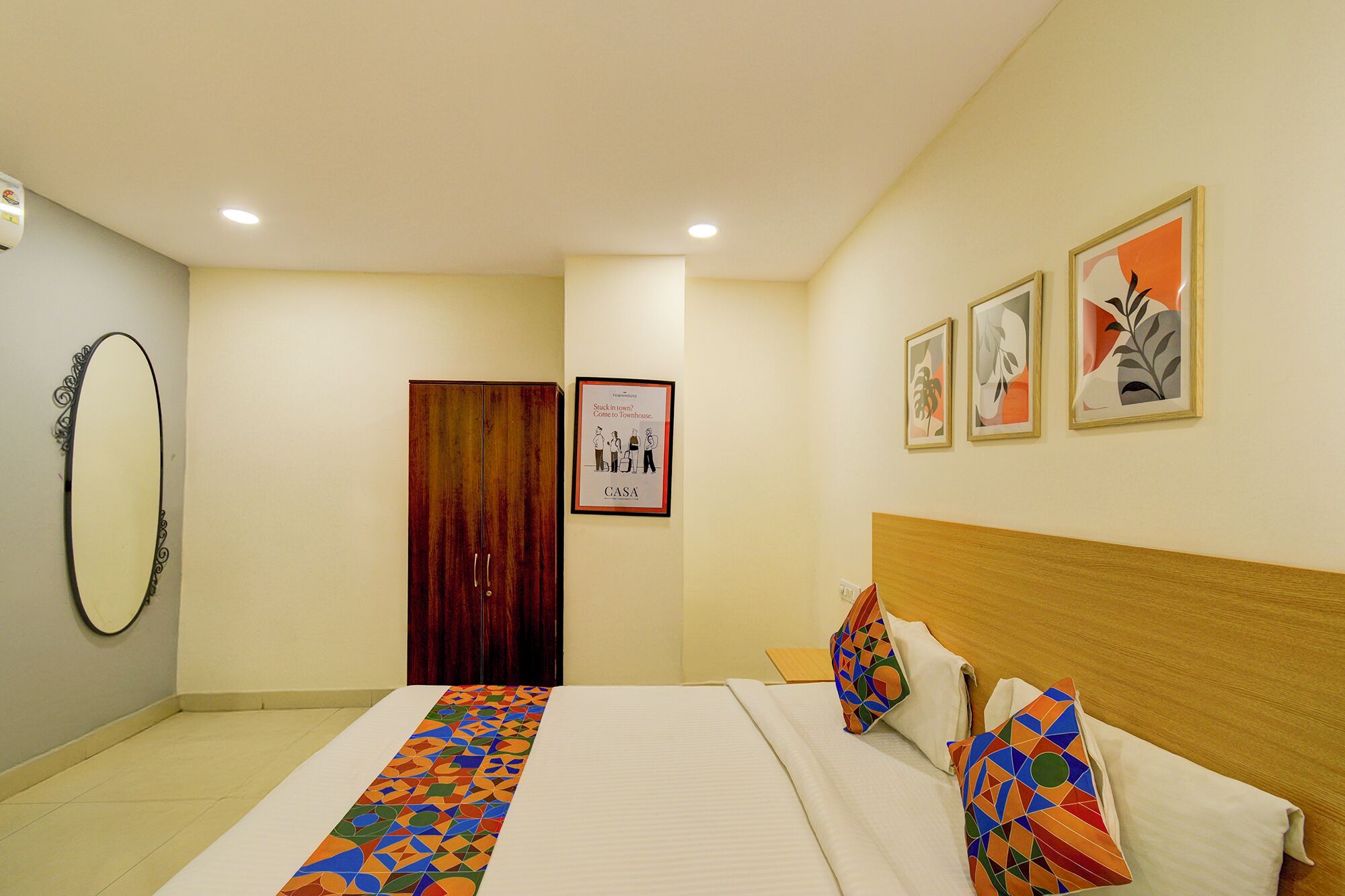 Une chambre d’hôtel avec un lit, une tête de lit en bois, un miroir, une porte et trois tableaux encadrés accrochés au mur.