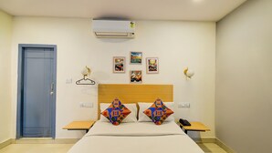 Ein Hotelzimmer mit Bett, Nachttischen, einem Kleiderschrank, einer Klimaanlage und Wandbildern.
