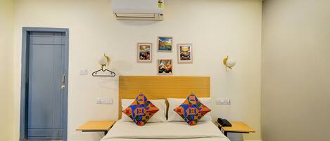 A hotel room with a bed, bedside tables, a wardrobe, an air conditioner, and wall-mounted artwork.