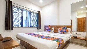 A modern hotel room with a large bed, a wooden headboard, a bedside table, a nightstand, a mirror, and a window with geometric curtains. - FabHotel Apple - Nr. by ITI (Indore)