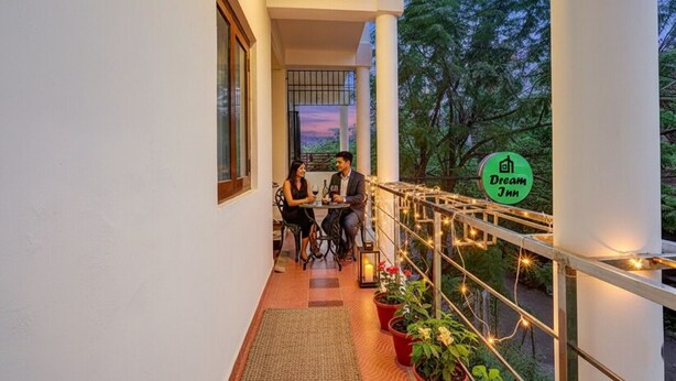 A balcony with a couple dining, surrounded by potted plants and string lights, with a view of trees and a sunset. - FabHotel Dream Inn - Mogappair East (Chennai)