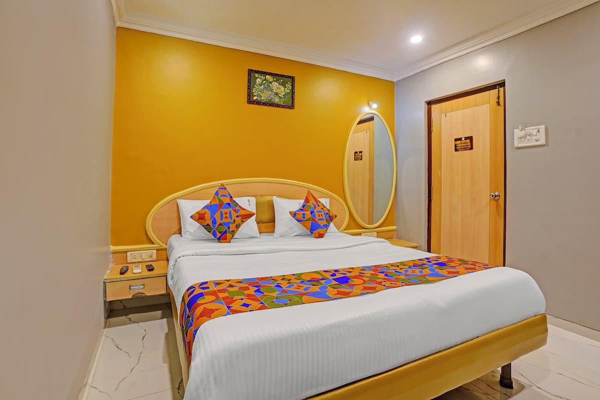 A hotel room with a bed, a nightstand, a mirror, and a door.