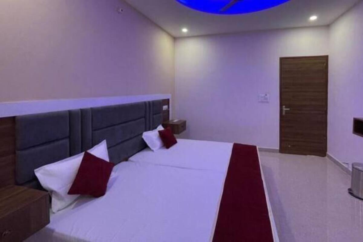 Une chambre d’hôtel moderne avec un grand lit, une tête de lit, une table de chevet, un téléviseur fixé au mur et une porte.
