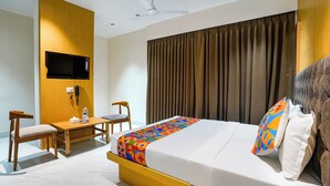 A hotel room with a bed, a desk, a chair, a television, and a window with curtains. - Fabhotel Gavalidev (Navi Mumbai)