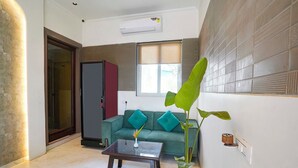 A living room with a sofa, a coffee table, a potted plant, and a window with blinds. - Fabhotel Gavalidev (Navi Mumbai)