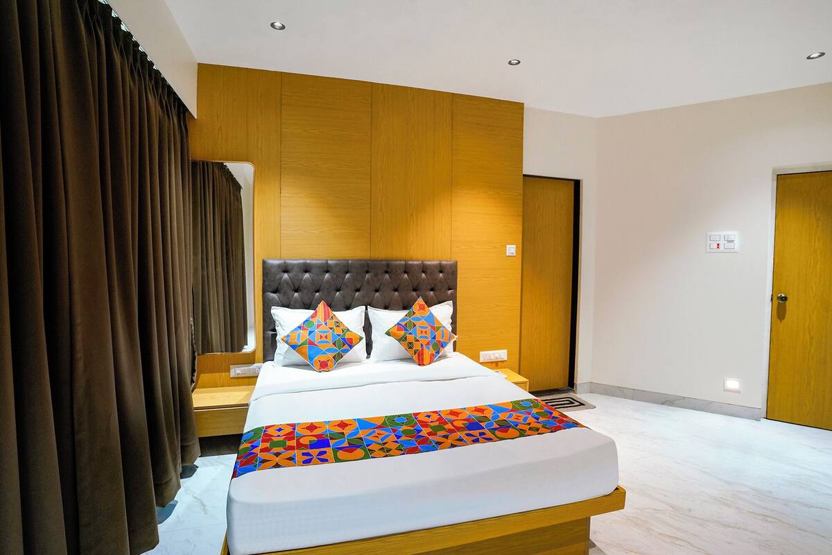 Une chambre d’hôtel moderne avec un grand lit, une tête de lit en bois et une couvre-lit aux motifs géométriques et aux couleurs vives.