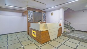 A hotel reception area with a reception desk, a ceiling fan, and a staircase leading to an upper floor. - Via Nobel Grand (Hyderabad)