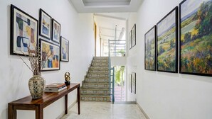 Un couloir avec un escalier, des œuvres d’art encadrées accrochées aux murs, et une console en bois sur laquelle sont posés des livres et un vase.