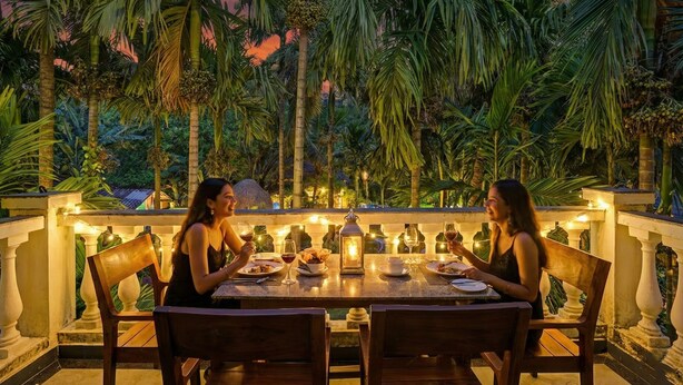 Deux personnes dînent à une table en plein air, avec vue sur des palmiers et un coucher de soleil.