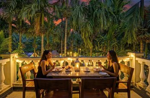 Two people dining at an outdoor table with a view of palm trees and a sunset. - Via Lavish Exotic (Arambol)