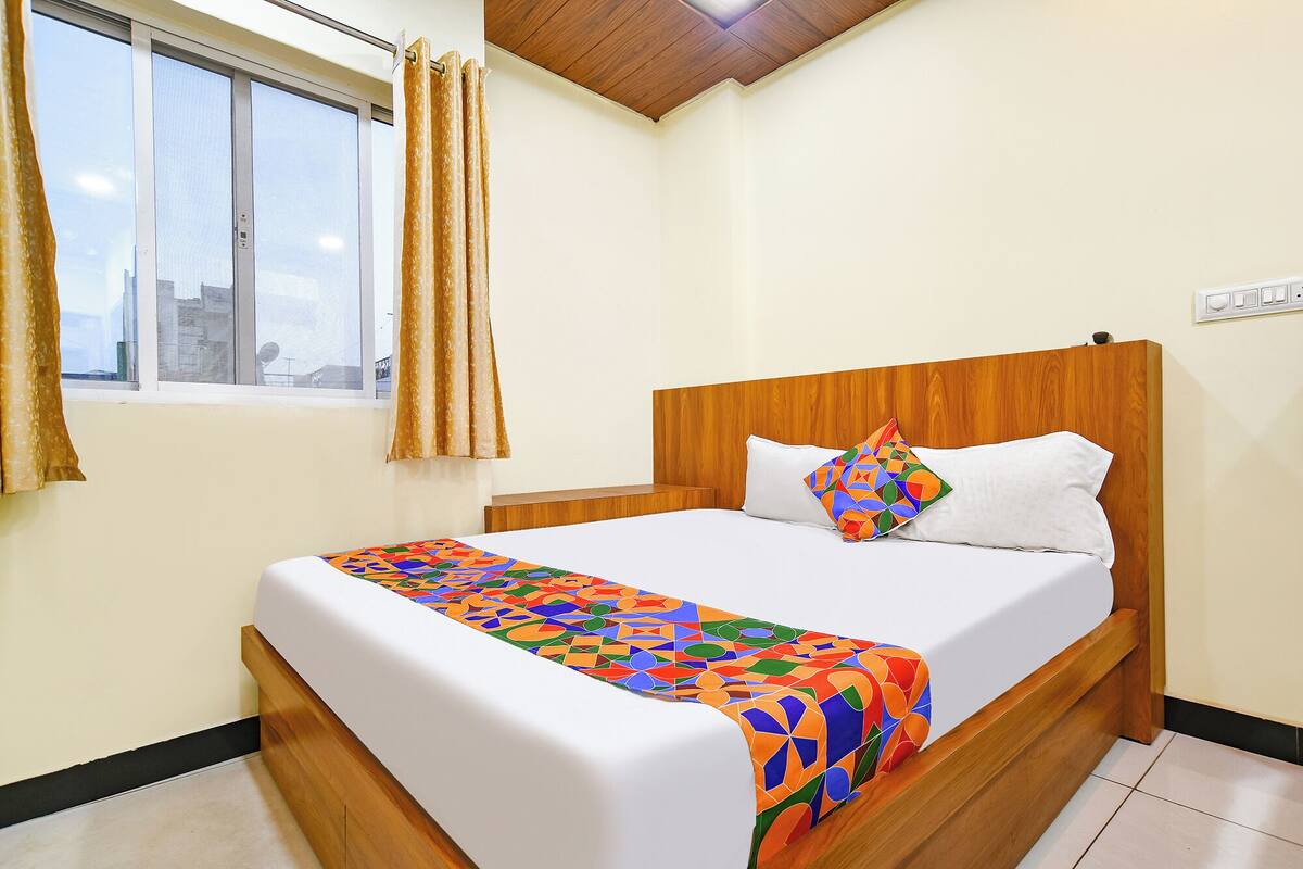 A neatly made bed with a colorful geometric-patterned bedspread, a white pillow, and a wooden headboard.