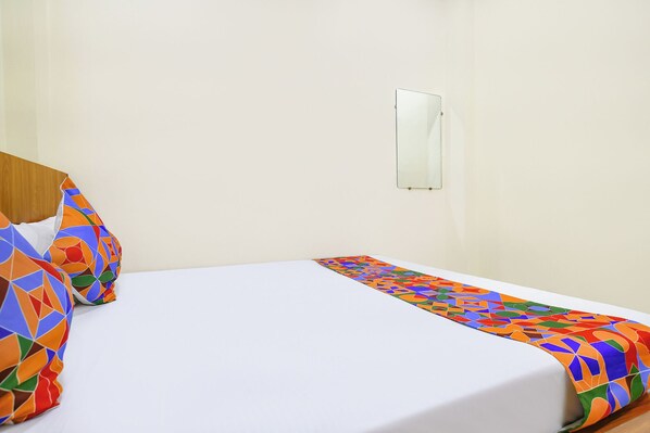 A hotel room with a single bed, a wooden headboard, and a colorful geometric-patterned bedspread. - Via Ratna Palace I (Ujjain)