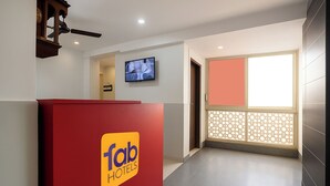 Un espace d’accueil d’hôtel avec un comptoir rouge sur lequel est affiché le logo de la chaîne « fab hotels », un téléviseur fixé au mur et une vue sur le hall d’entrée, agrémenté d’une cloison décorative.