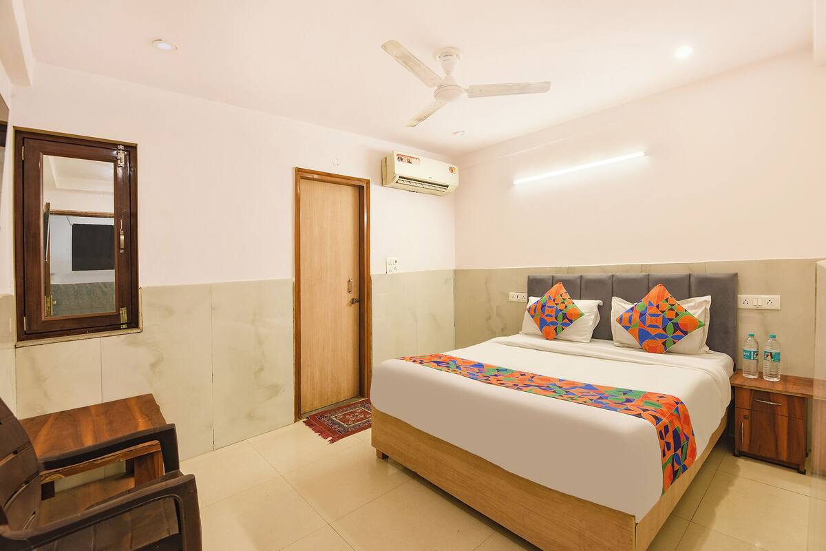 Habitación de hotel con cama, una silla de madera, ventilador de techo, unidad de aire acondicionado y mesita de noche con botellas de agua.