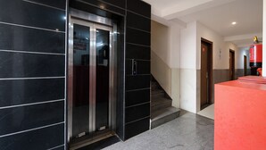 Un ascenseur moderne avec une porte en verre, un escalier et un comptoir d’accueil rouge.