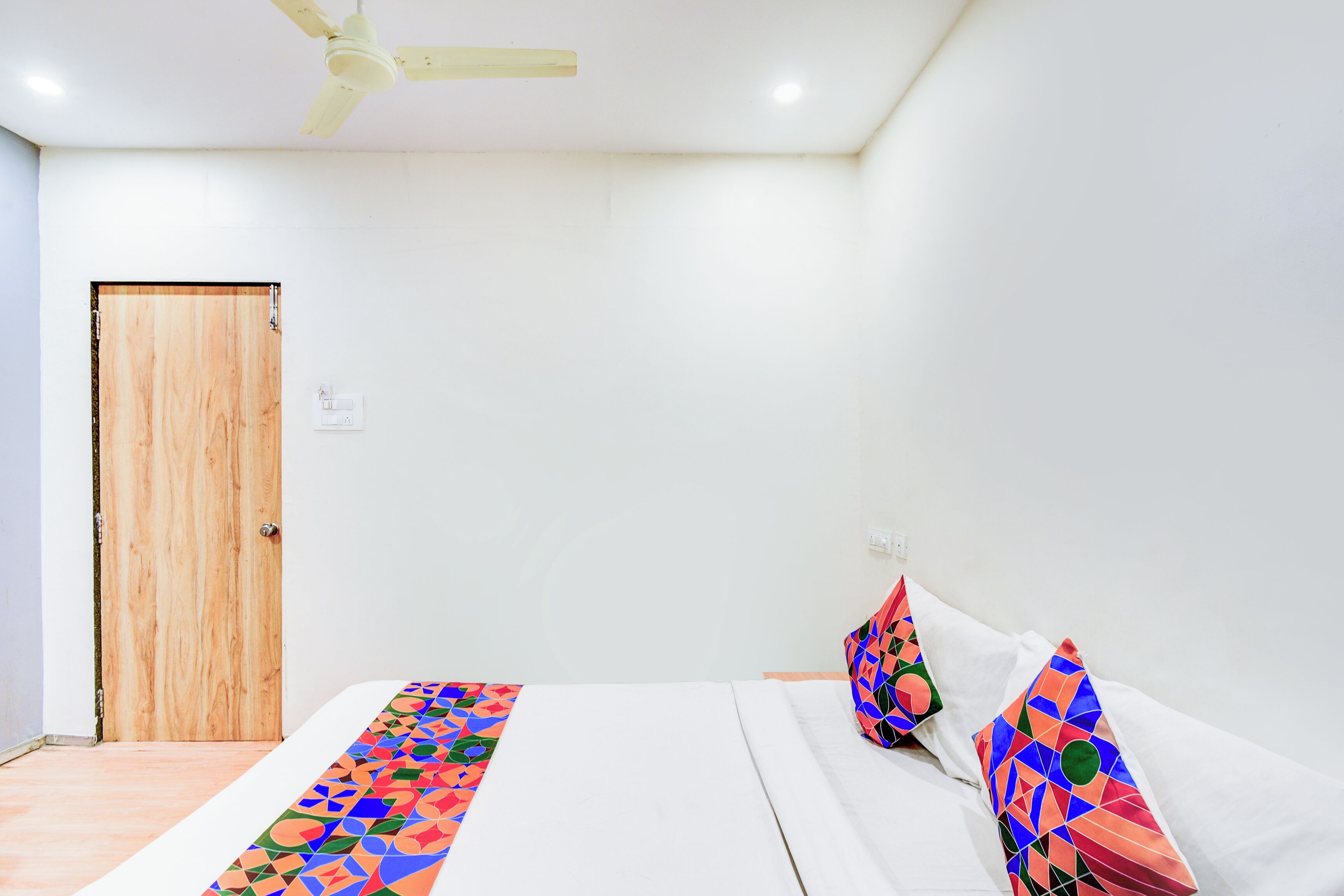 A room with a wooden door, a bed with colorful bedding, and a ceiling fan.