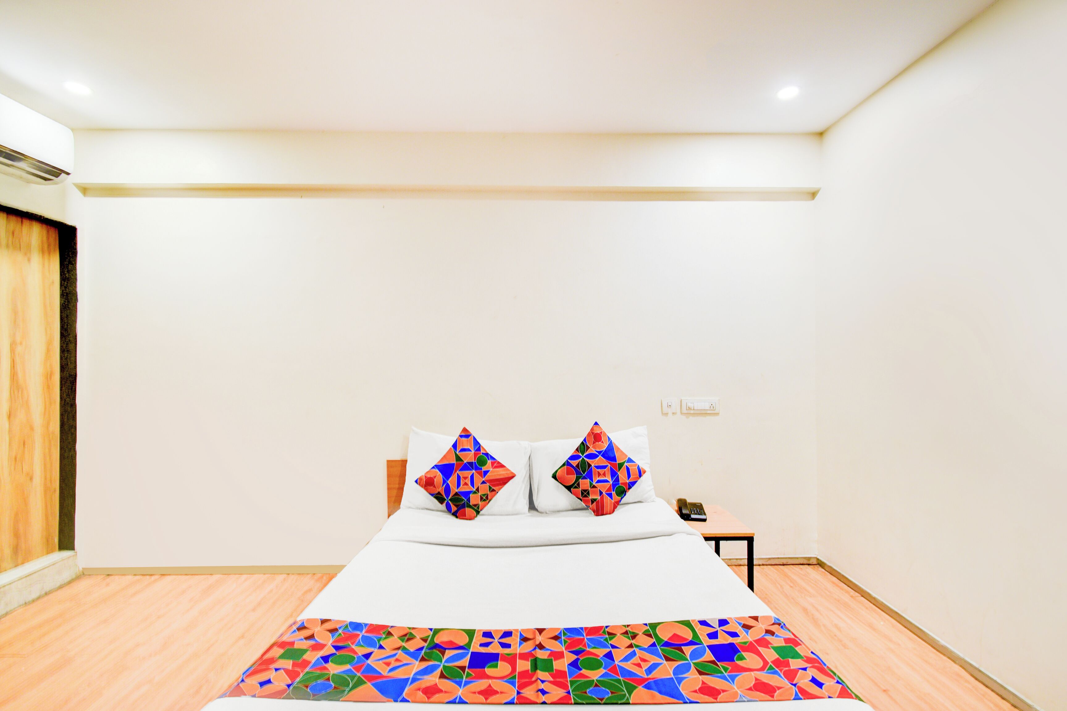A hotel room with a bed, two pillows, a bedside table, and a patterned rug.